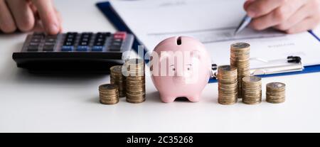 Der Unternehmer Hand mit Taschenrechner mit Gestapelte Münzen und Sparschwein auf hölzernen Schreibtisch Stockfoto