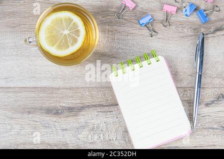 Ein offenes Notizbuch auf einem Holztisch, daneben stehen ein silberner Stift und eine Tasse Minztee mit Zitrone. Stockfoto