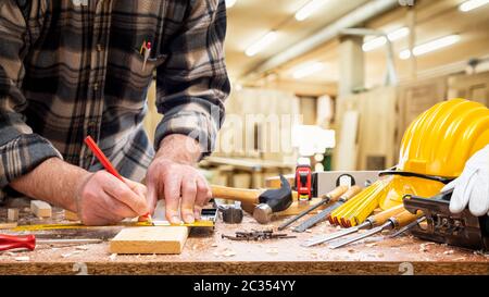 Nahaufnahme. Tischler mit Bleistift und Tischlerplatz zeichnen die Schnittlinie auf einem Holzbrett. Bauindustrie, Zimmerei. Stockfoto