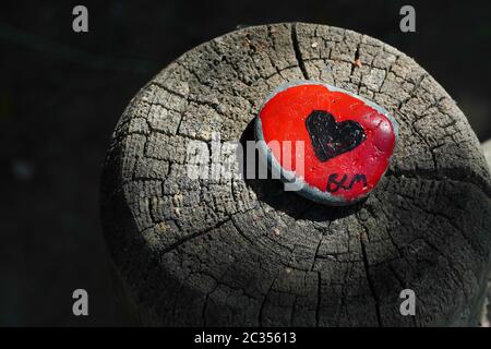 Ein kleiner, flacher, rot bemalter Stein mit einem schwarzen Herzen, der an die BLM- oder Black Lives Matter-Bewegung erinnert. Wurde auf einen hölzernen Zaunpfosten gestellt, sonnenbeschienenen. Stockfoto