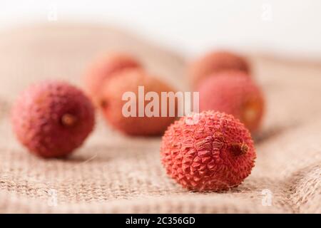 Nahaufnahme einer kleinen Gruppe von Früchten (Lichi) des Lychee-Baumes (Litchi chinensis) auf grobem Sack-Leinentuch. Der Fokus liegt auf dem Vordergrund. Stockfoto