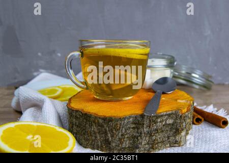Glas transparente Tasse mit Minztee steht auf einem Holzständer, neben einer Zuckerdose mit Zuckerwürfeln, in Scheiben geschnittene Zitrone und einem Löffel. Stockfoto
