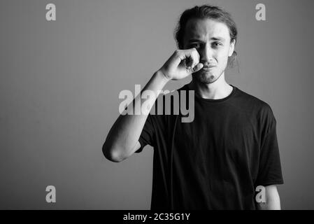 Junger, schöner Mann mit schwarzem Hemd vor grauem Hintergrund Stockfoto