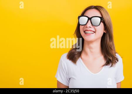 Portrait Asian Thai schöne junge Frau glücklich lächelnde weiße Zähne mit Sonnenbrille und Blick auf die Seitenfläche, Studio isoliert auf gelbem Hintergrund, Stockfoto