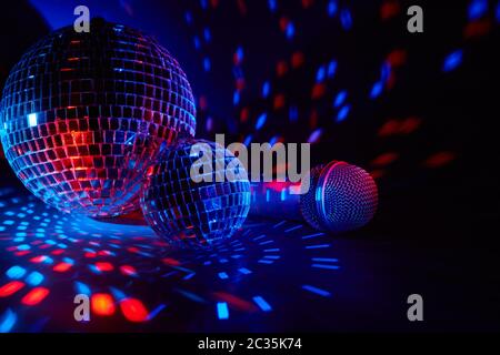 Glitzernde Spiegel Disco Kugeln und Mikrofon auf dunklem Hintergrund mit rot-blauer Beleuchtung. Kopierbereich. Wochenende oder Feiertagsparty. Karaoke-Club. Für adver Stockfoto