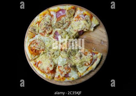 Pizza mit Salami, Mozzarella, Tomaten, Bananen steht auf einem Holzbrett, auf dem schwarzen Hintergrund isoliert auf schwarzem Hintergrund. Top Ansichten witch klar Stockfoto