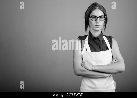 Junge Frau mit Schürze und Brille vor grauem Hintergrund Stockfoto