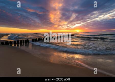 Schöner Sonnenuntergang an der Ostsee, Wellen waschen die alten hölzernen Wellenbrecher Stockfoto