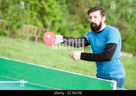 Der bärtige Spieler spielt Tischtennis als Erholung im Freien im Park. Stockfoto