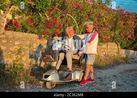 Seniorenpaar, das entlang der Promenade an der Adria spazierengeht - behinderter Mann im Rollstuhl Stockfoto