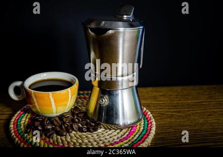 Orangefarbene und gelbe Kaffeetasse mit Kaffeekanne auf einem Tisch und dunklem Hintergrund Stockfoto