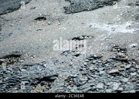 Halb zerstörte holprige Asphalt, alte Technologie der Straßenproduktion. Gefahr bei hoher Geschwindigkeit. Löcher, Schlaglöcher, Granularität Stockfoto