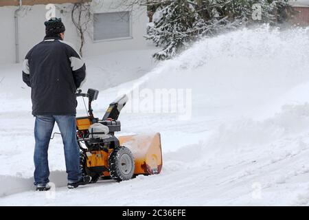 Ein Mann räumt die Straße und den Bürgersteig mit einem Schneegebläse Stockfoto