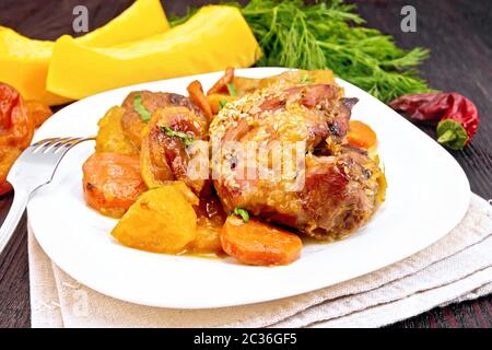 Hühnereintopf mit Kürbis, getrockneten Aprikosen, Karotten und Rotwein, bestreut mit Sesamsamen auf einem Teller auf Serviette gegen dunkles Holzbrett Stockfoto