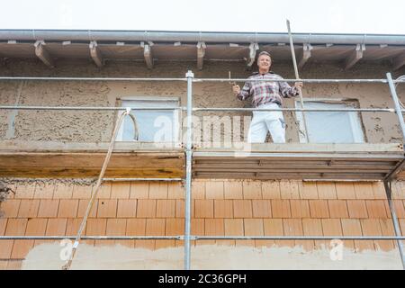 Gipser auf Gerüst auf der Baustelle mit Blick in die Kamera Stockfoto