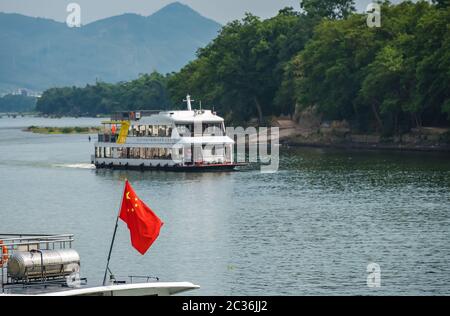 Guilin, China - August 2019: Rote chinesische Nationalflagge flattern auf einem Mast auf dem Deck der Sightseeing boatt voll von Touristen, die auf einer Reise auf Stockfoto