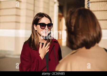 Porträt einer jungen lächelnden Dame in Sonnenbrille stehen und glücklich mit Freund auf der Straße sprechen Stockfoto