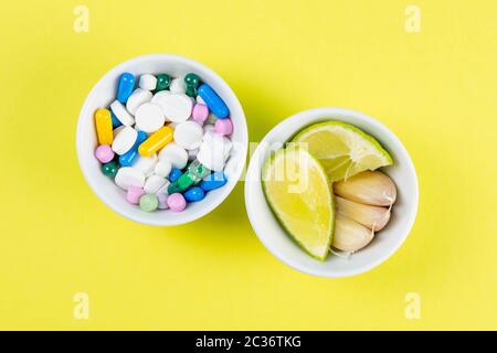 Limette und Ingwer gegen mehrfarbige Tabletten. Das Konzept der Wahl einer gesunden Ernährung gegenüber der Einnahme von Medikamenten. Von oben mit viel Platz. Stockfoto