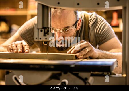 Detail eines Zimmermanns Absicht auf einem Stück Holz mit Präzision mit einer Bandsäge. Stockfoto