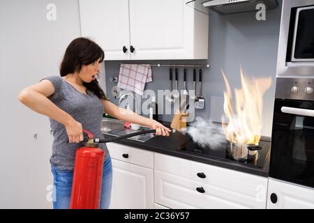 Frau mit Feuerlöscher zu stoppen Feuer zum Brennen von kochenden Topf in der Küche Stockfoto