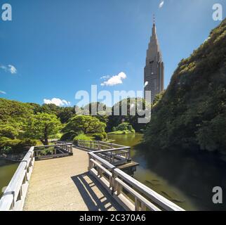 Shinjuku's Docomo Turm mit Blick auf den oberen Teich Zickzack-förmigen Brücke und die Kiefer und Ahorn für Stockfoto