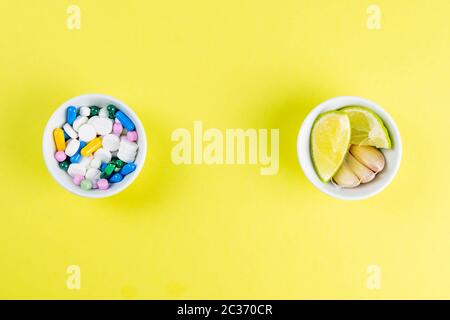 Limette und Ingwer gegen mehrfarbige Tabletten. Das Konzept der Wahl einer gesunden Ernährung gegenüber der Einnahme von Medikamenten. Von oben mit viel Platz. Stockfoto