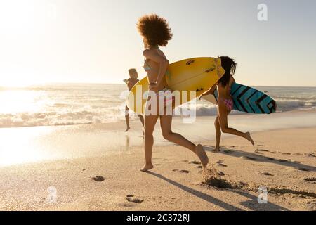 Junge Frauen mit gemischtem Rennen halten Surfbretter am Strand Stockfoto