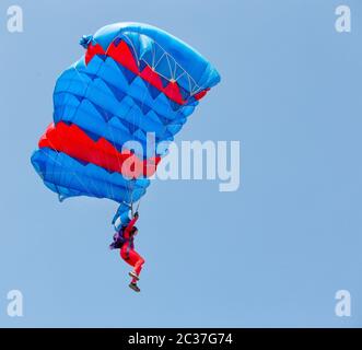 Fallschirmjäger in roten Anzug steigt unter dem Vordach von Fallschirm in den blauen Himmel. Stockfoto