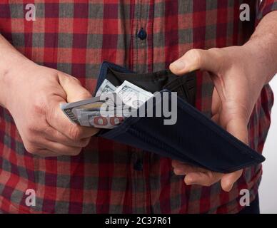 Mann in einem karierten roten Hemd hält eine Brieftasche voller hundert US-Papier-Dollar-Banknoten, Begriff des Gehalts, Vermögen Stockfoto