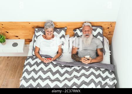 Happy Senior paar mit mobilen Smartphones unter Decken im Bett - ältere Menschen mit lustigen Bett Zeit beobachten auf neue Medien Trends Stockfoto