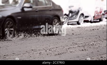 Ein Auto, das auf der Stadtstraße mit geschmolzenem und schmutzigem Schnee bedeckt Stockfoto