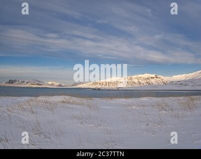 Eine verschneite Wiese an der Küste Islands mit Bergen im Hintergrund Stockfoto