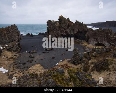 Zerklüftete Lavafelsen an einem schwarzen Sandstrand in Island Stockfoto