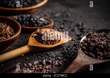 Verschiedene schwarze Salze in Löffeln auf dunklem Hintergrund Stockfoto