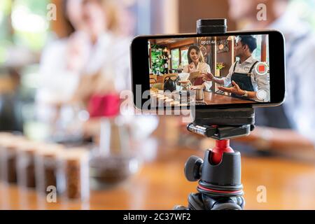 VLOG von jungen erwachsenen Asiatischen Eigentümer Unternehmer bewerten cafe Coffee Shop und Leben in sozialen Medien für Online Marketing mit Smart Phone im Cafe. Mit fo Stockfoto
