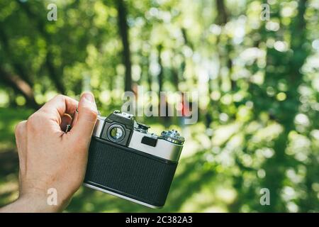 Die Hand eines Mannes hält eine alte Vintage-Filmkamera und fotografiert eine grüne Landschaft. Ego-Blick POV Stockfoto