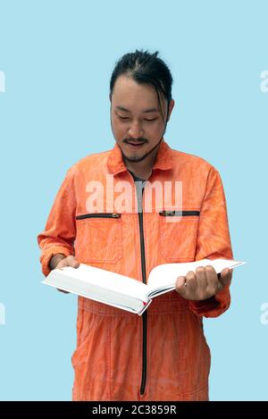 Der Hauptmechaniker in der orangen Uniform, der das große Buch hält. Stellen Sie sich auf und lesen Sie das Wartungshandbuch sorgfältig durch. Porträt mit Studiolicht. Stockfoto