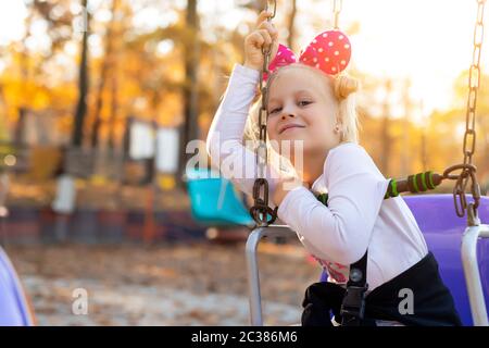 Kleine niedliche liebenswert kaukasischen blonde Schulmädchen genießen Spaß sitzen und Reiten alte Kette Schaukel Karussell in der Stadt Themenpark. Glücklich Stockfoto