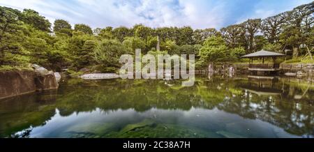 Zentraler Teich des Mejiro Garden, der von großen flachen Steinen unter dem Laub der Momi umgeben ist Stockfoto