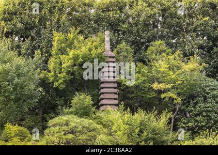 Steinturm Pagode vor dem zentralen Teich des Mejiro Garden, der von großen Wohnungen umgeben ist Stockfoto