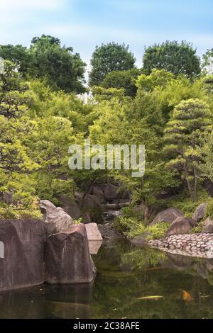 Wasserfall fließt in den zentralen Teich des Mejiro Garden, wo Karpfen schwimmen und die umgeben ist Stockfoto