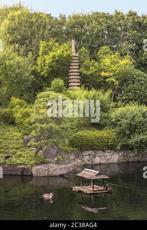 Steinturm Pagode vor dem zentralen Teich des Mejiro Garden, der von großen Wohnungen umgeben ist Stockfoto
