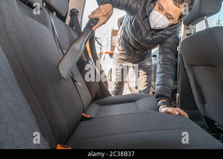 Saugen Sie das Innere eines Pkw mit einem industriellen Staubsauger. Man arbeitet in schützender medizinischer Maske. Schutz gegen Coronavirus. Stockfoto