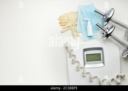 Sportgeräte, Waagen, medizinische Masken und Desinfektionsmittel auf weißem Hintergrund. Draufsicht, Kopierbereich. Fitness. Ausgabezeitraum. Gewicht und Gesundheitskontrolle Stockfoto