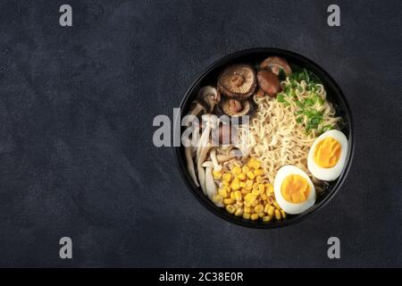 Ramen. Soba-Nudeln mit Eiern, Shiitake und Enoki-Pilzen und Gemüse, von oben auf dunklem Hintergrund mit Copyspace geschossen Stockfoto