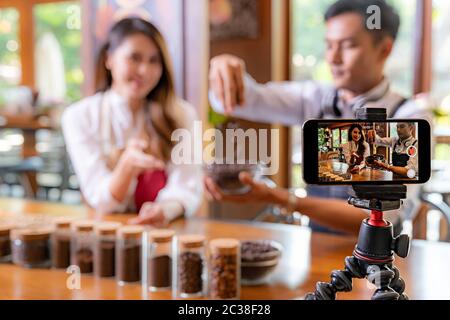 VLOG von jungen erwachsenen Asiatischen Eigentümer Unternehmer bewerten cafe Coffee Shop und Leben in sozialen Medien für Online Marketing mit Smart Phone im Cafe. Mit fo Stockfoto