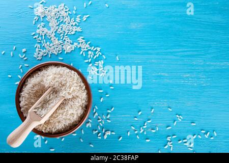 Ton Schüssel mit Reis und einem Holzspachtel auf blauem Hintergrund. Blick von oben. Das Konzept der gesunde natürliche Lebensmittel. Stockfoto