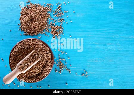 Ton Schüssel mit Buchweizen und einem Holzspachtel auf blauem Hintergrund. Blick von oben. Das Konzept der gesunde natürliche Lebensmittel. Stockfoto