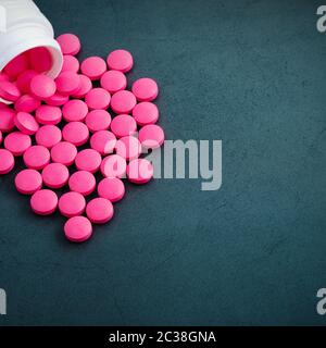 Rosa helle Pillen sind aus einem weißen Glas auf einem grauen Hintergrund verstreut. Bank und Tabletten in der oberen linken Ecke des Bildes.. Stockfoto