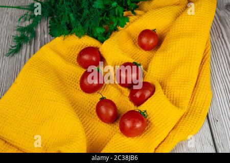 Kirschtomaten mit Kräutern auf einem gelben Handtuch stehen auf einem Holztisch Stockfoto